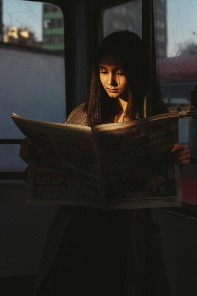 A young woman reading a newspaper in a Minsk tram with soft light highlighting her face.